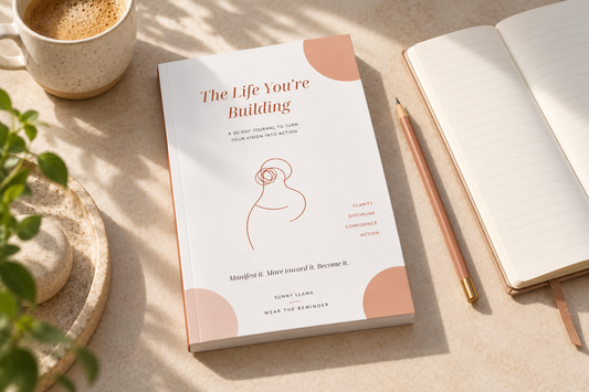 The Life You’re Building 30-day journal with its updated white and terracotta cover, beside a notebook and pencil